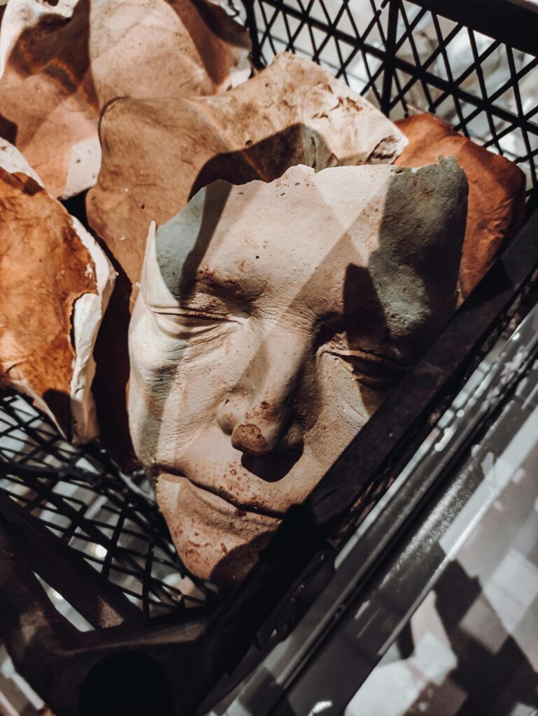 A basket filled with broken clay masks depicting human faces, casting shadows.