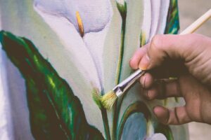 Close-up view of an artist painting a floral design on canvas using a brush.